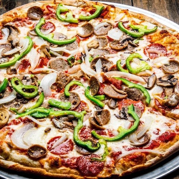 A whole pizza with pepperoni, sausage, mushrooms, onions, and green peppers on a metal tray.