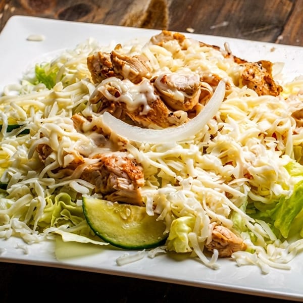 A white rectangular plate holds a salad with chicken, shredded cheese, lettuce, zucchini, and onions.