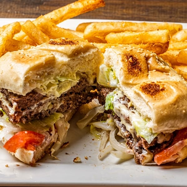 A large burger cut in half, revealing meat, cheese, lettuce, tomato, and onion, served with fries.