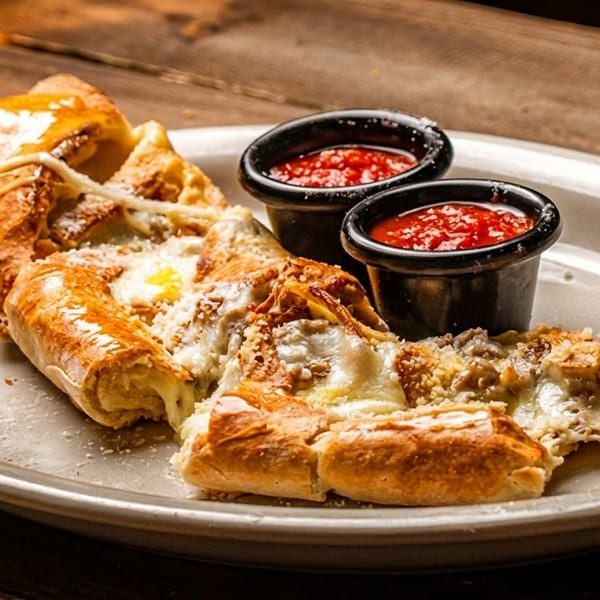 Cheesy calzone with melted cheese and parmesan, served with two small cups of marinara sauce.